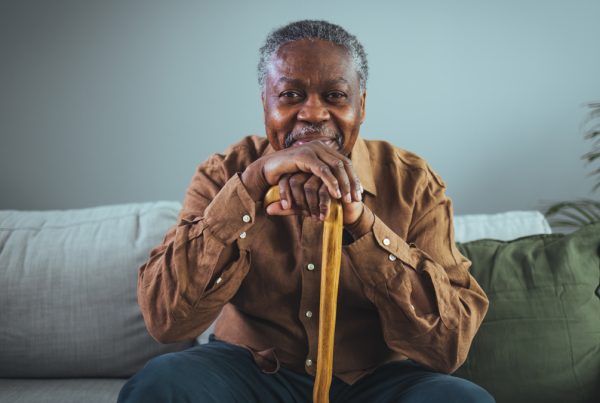 Elderly man sitting on couch and resting his head on his cane