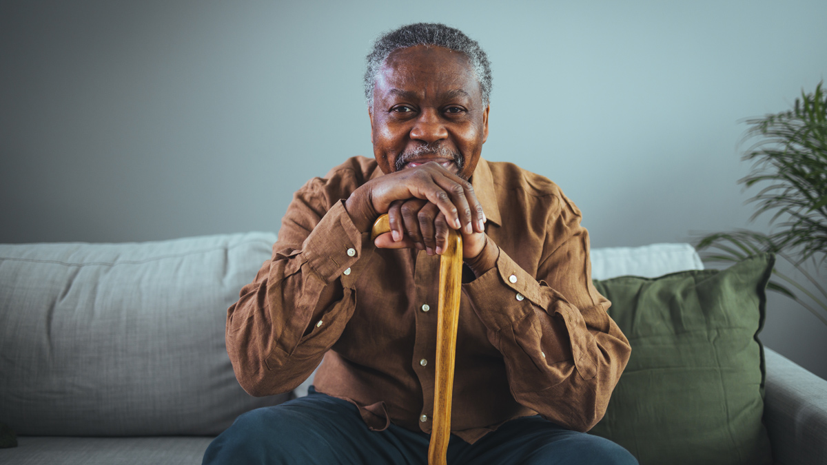 Elderly man sitting on couch and resting his head on his cane