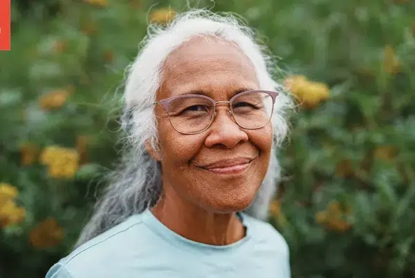 Senior woman with glasses smiling in front of flowers