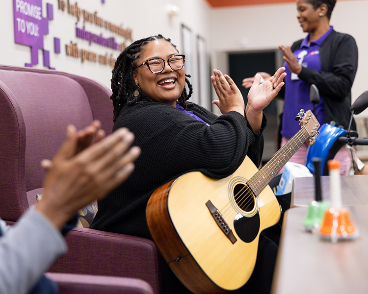 Woman holding guitar clapping and smiling